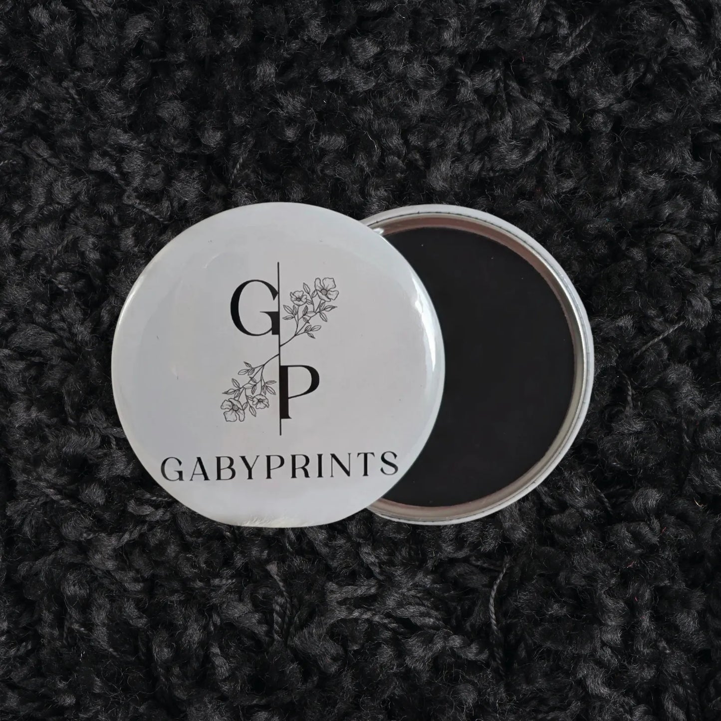 Aimant promotionnel blanc à l'effigie de GabyPrints sur tissus noir – White logo magnet featuring GabyPrints on black fabric