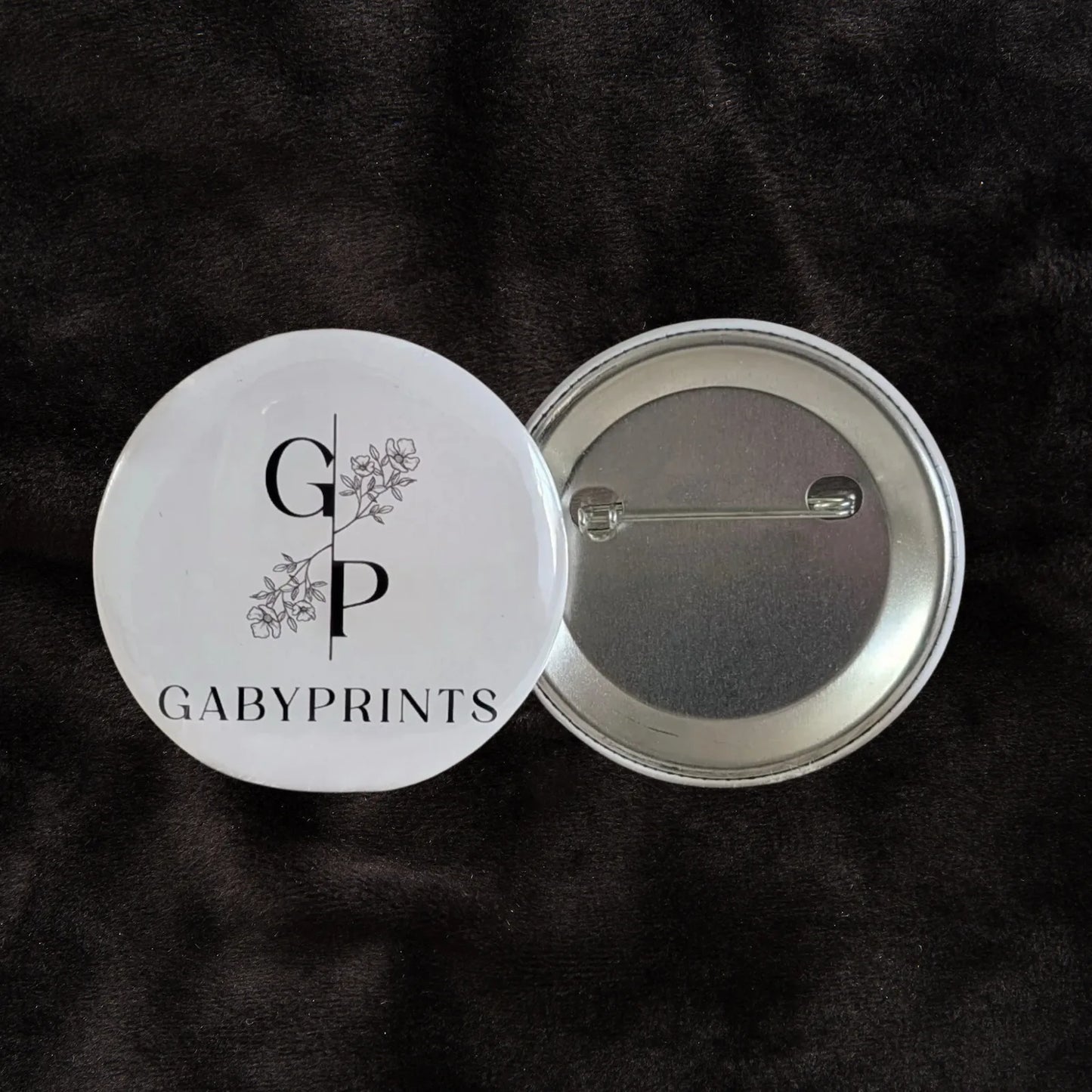 Macaron promotionnel blanc à l'effigie de GabyPrints sur tissus noir – White promotional button featuring GabyPrints on black fabric