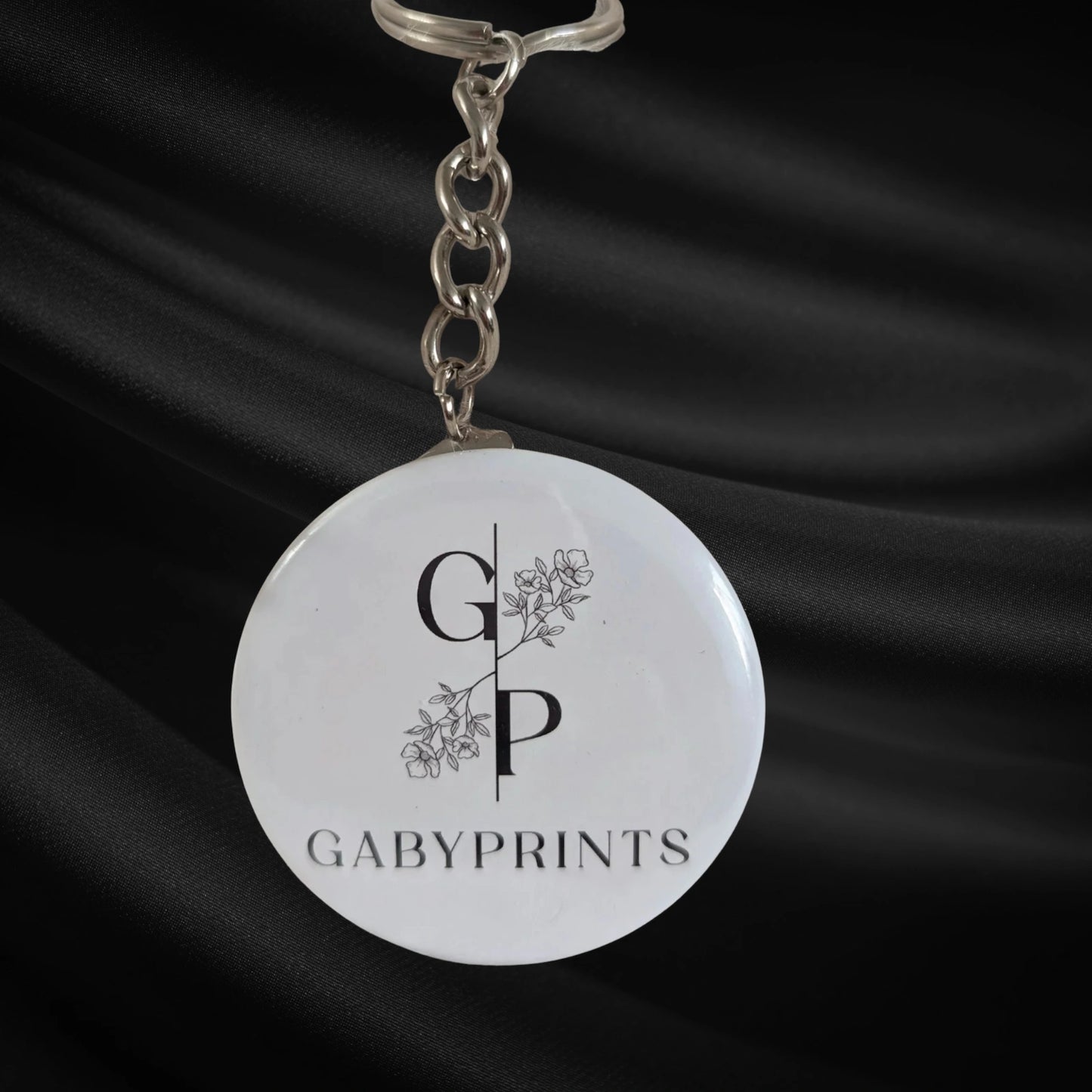 Porte-clé promotionnel blanc à l'effigie de GabyPrints sur tissus noir – White branded keychain featuring GabyPrints on black fabric