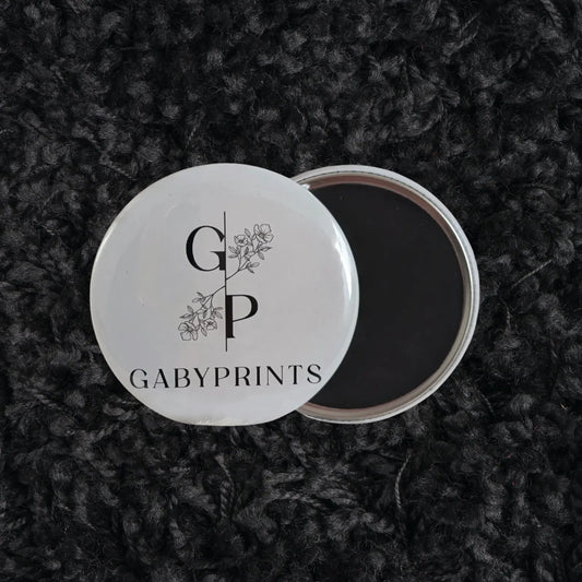 Aimant promotionnel blanc à l'effigie de GabyPrints sur tissus noir – White logo magnet featuring GabyPrints on black fabric